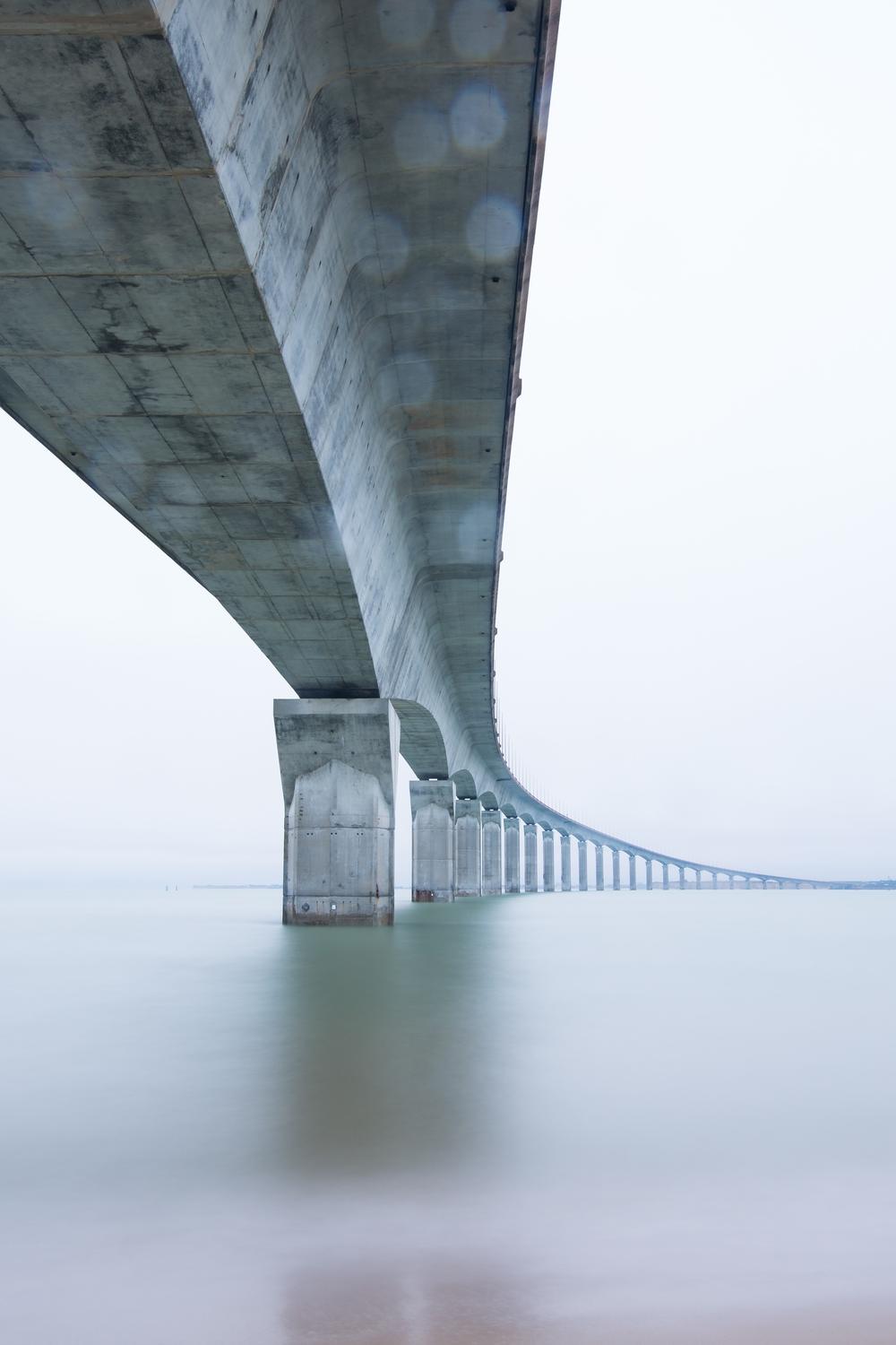 Impalcato di un viadotto in cemento armato visto dal basso, con le pile che si rincorrono fino all’orizzonte